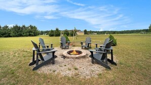 A fire pit with four Adirondack chairs arranged around it in an open grassy area. - Hot Tub! | Pet Friendly! | Game Room! (Traverse City)