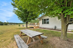 A picnic table in a grassy area with a house and a tree in the background. - Hot Tub! | Pet Friendly! | Game Room! (Traverse City)