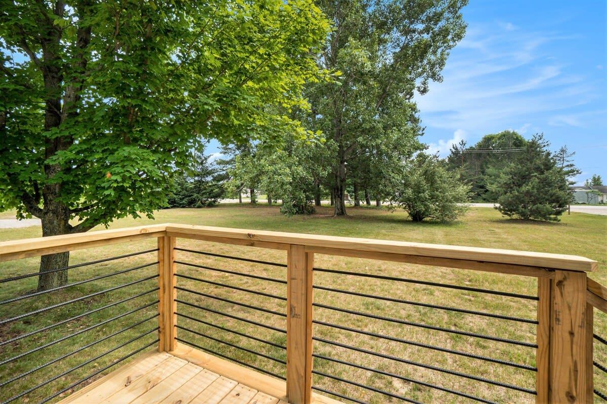Um deck de madeira com guarda-corpo de metal, com vista para uma área gramada e árvores.