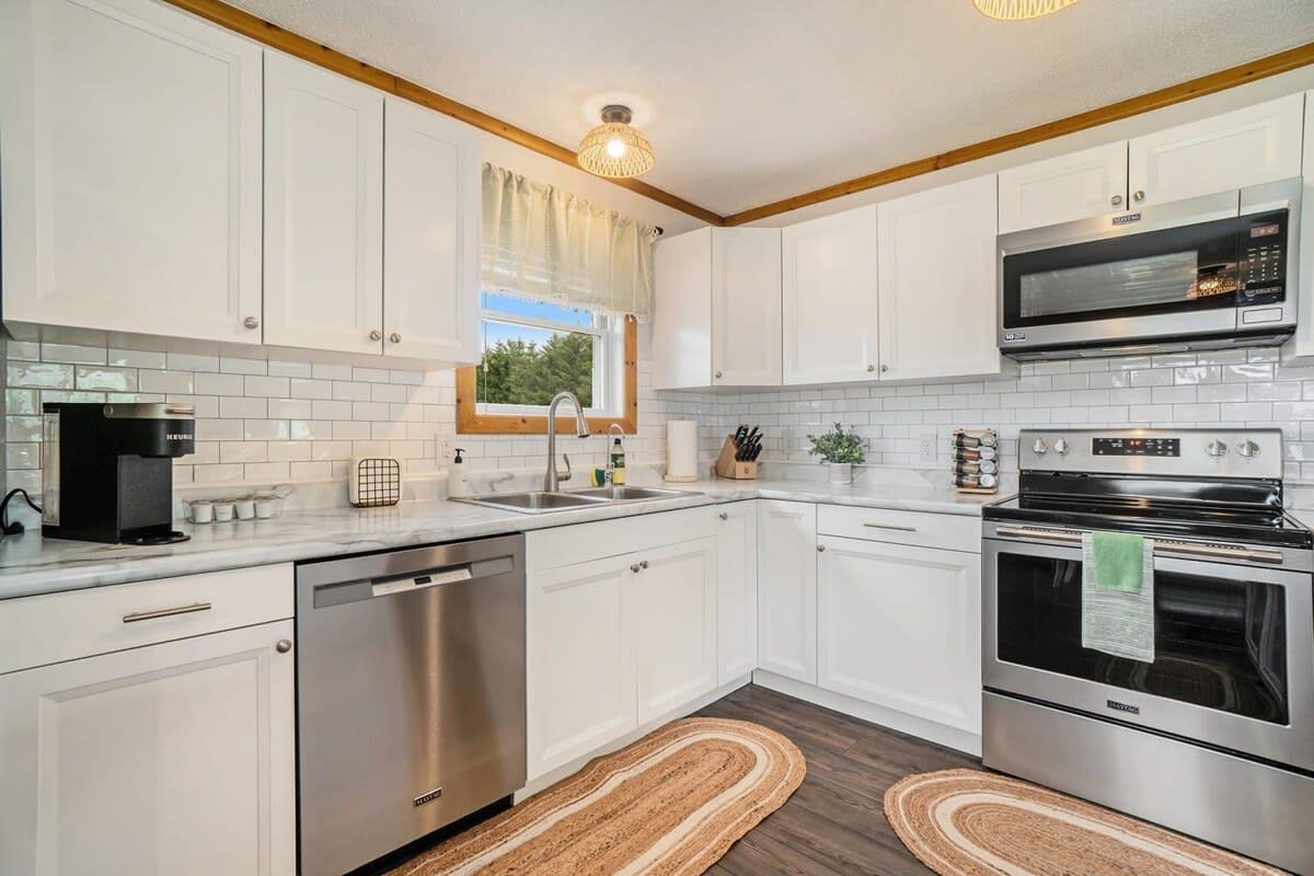 A modern kitchen with white cabinets, stainless steel appliances, and a window with a view.