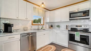 A modern kitchen with white cabinets, stainless steel appliances, and a window with a view.