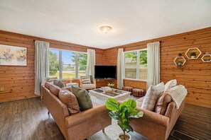 A cozy living room with a brown leather sofa, a flat-screen TV, and a coffee table. - Hot Tub! | Pet Friendly! | Game Room! (Traverse City)