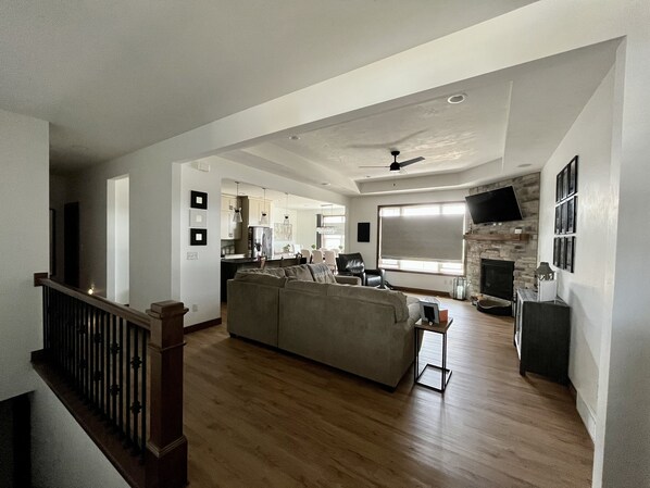 A spacious living room with a large sofa, a fireplace, and a television mounted on the wall.