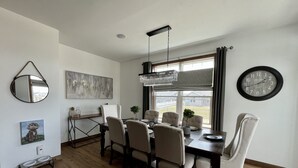 A dining area with a wooden table, six chairs, a chandelier, a clock, and artwork on the walls. - Entire house oasis for EAA (Appleton)