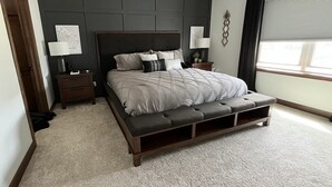 A bedroom with a large bed, two bedside tables, a nightstand, a window with blinds, and a dark headboard. - Entire house oasis for EAA (Appleton)