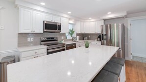 A modern kitchen with white cabinetry, stainless steel appliances, and a large island with seating. - Spacious Retreat With Pool, Game Room & Fireplace | Sleeps 10 | Backyard Oasis & Screened Gazebo | Family-Friendly Getaway | 24/7 Hospitality (Plymouth)