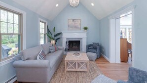A spacious living room with a fireplace, a sofa, a coffee table, and a chandelier. - Spacious Retreat With Pool, Game Room & Fireplace | Sleeps 10 | Backyard Oasis & Screened Gazebo | Family-Friendly Getaway | 24/7 Hospitality (Plymouth)