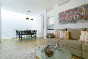 Een moderne woonkamer met een glazen salontafel, een beige bank met gestreepte kussens, en een eetgedeelte met een tafel en stoelen.