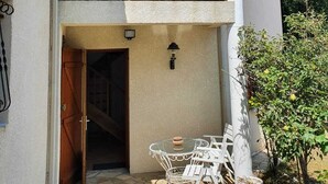 Ein zweistöckiges Gebäude mit Balkon, einem gepflasterten Eingangsbereich und Gartenmöbeln.