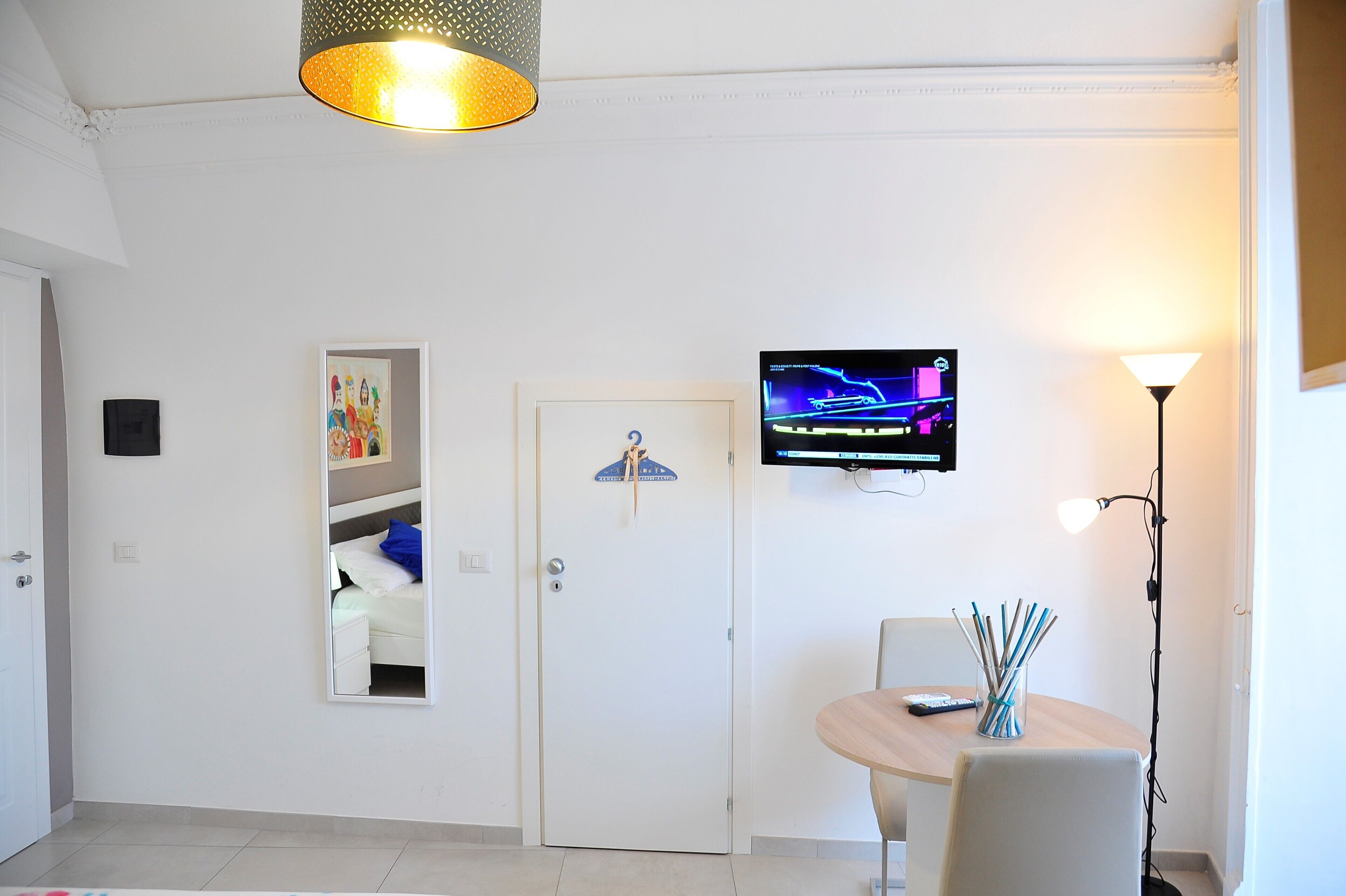 A hotel room with a bed, a TV mounted on the wall, a desk with a chair, and a lamp.