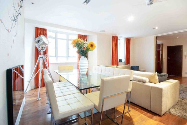 Ein modernes Wohnzimmer mit einem Glastisch, weißen Sofas und einem großen Fenster mit Vorhängen.