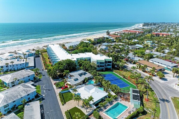An aerial view of a coastal hotel with multiple buildings, a swimming pool, and a beach in the background.