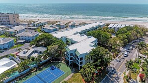 Un hôtel situé sur la côte, composé de plusieurs bâtiments, doté d’un court de tennis et offrant une vue sur la plage.