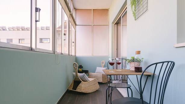 Varanda com cadeiras de vime, uma mesa e um vaso de planta.