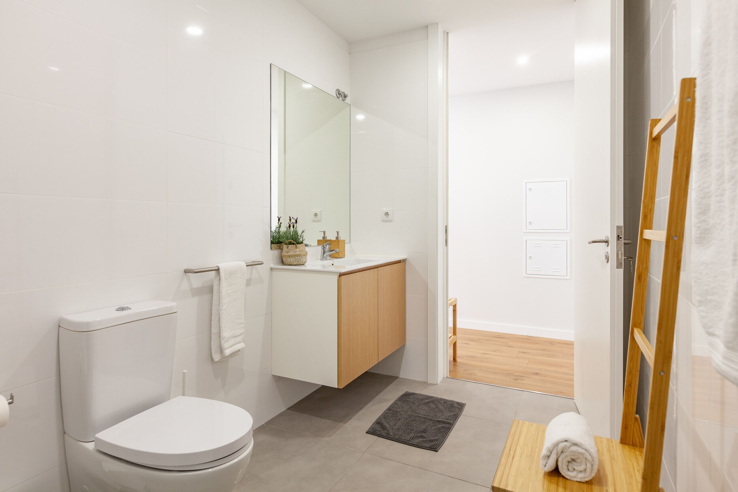 A modern bathroom with a toilet, sink, mirror, and wooden floor.