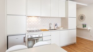 A modern kitchen with white cabinetry, a built-in brick backsplash, a countertop with a sink, and a small refrigerator.