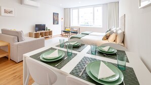 A modern living room with a dining area, a sofa, a TV, and a large window.