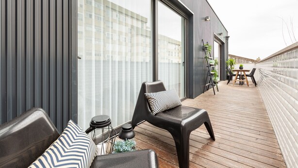 A modern outdoor deck with a wooden floor, a black chair with a patterned cushion, a small round table, and a potted plant. - Oporto Palace Apartments Five (Oporto)