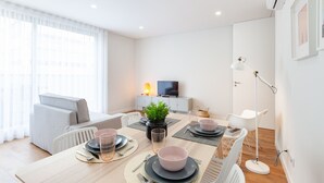 A modern dining area with a wooden table set for four, a sofa, a TV, and a floor lamp. - Oporto Palace Apartments Five (Oporto)