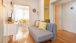 A modern living room with a grey sofa, yellow cushions, a wooden floor, and a dining area in the background. - D&S - Ribeira Premium Apartments I (Oporto)
