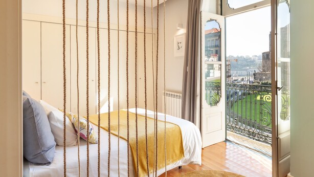 A bedroom with a bed, a view of the city through a balcony, and a window with curtains. - D&S - Ribeira Premium Apartments I (Oporto)