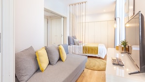 A modern bedroom with a bed, a sofa, a desk, and a TV. - D&S - Ribeira Premium Apartments I (Oporto)
