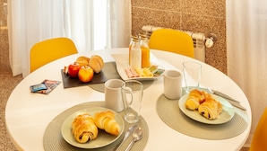 A breakfast setting with croissants, apples, orange juice, and a magazine on a round table. - D&S - Ribeira Premium Apartments I (Oporto)
