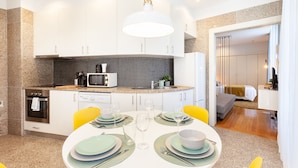 A modern kitchen with white cabinets, a microwave, and a dining area set with plates and glasses. - D&S - Ribeira Premium Apartments I (Oporto)