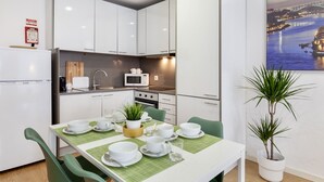 A modern kitchen with white cabinets, a microwave, and a sink. There is a dining table set with white plates, bowls, and a potted plant.