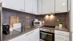 A modern kitchen with white cabinets, a stainless steel sink, a microwave, and an oven.