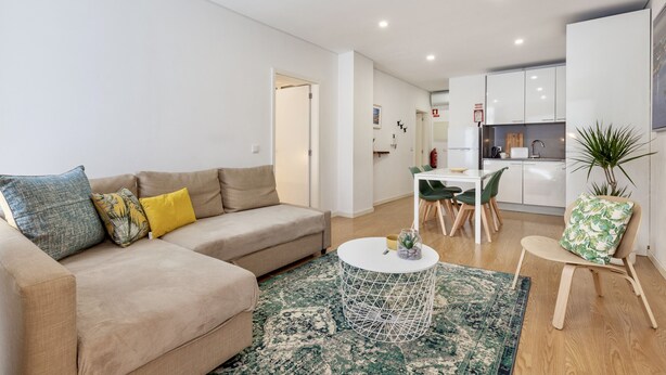 A modern living room with a sofa, coffee table, and a dining area with chairs and a table.