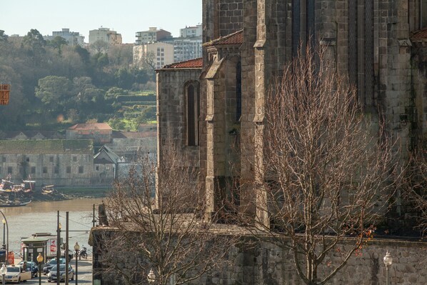 A historic stone building with arched windows and a tower, overlooking a river with boats.