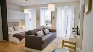 Un dormitorio moderno con cama, sofá, mesa de comedor con platos y cubiertos, y ventana con cortinas.