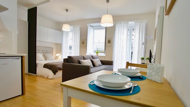 Una habitación de hotel moderna con cama, sofá, mesa de comedor con platos y cubiertos, y una pequeña cocina.