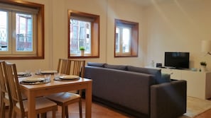 A dining area with a wooden table set for four, a grey sofa, and a television on a stand.