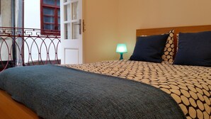 Une chambre à coucher avec un lit, une table de chevet avec une lampe, une fenêtre donnant sur un beau paysage et un balcon avec une balustrade.