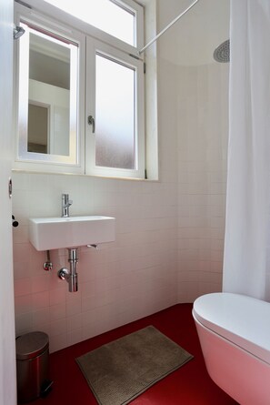 Un baño con lavamanos blanco, inodoro, cortina de ducha y un pequeño cubo de basura.