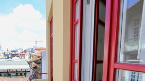 Ein schmaler Balkon mit roten Geländern und rotem Boden, mit Blick auf eine Stadtlandschaft mit Gebäuden und einer Baustelle.