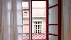 Eine offene Tür führt zu einem Balkon mit roter Brüstung und Blick auf ein Gebäude mit Balkonen.