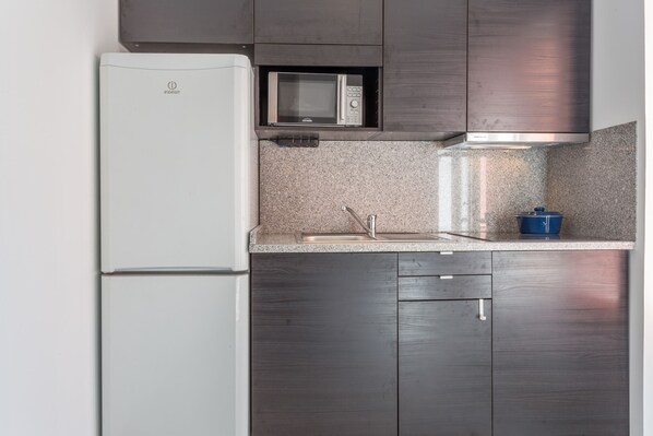 A kitchen with a white refrigerator, a microwave, and dark wooden cabinets. - Alves da Veiga Apartments I (Oporto)