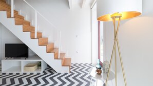 Una sala de estar moderna con una escalera, una lámpara de pie y un televisor sobre un mueble blanco.