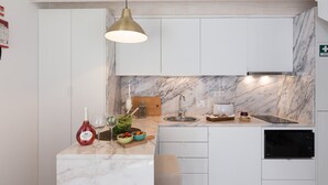 Una cocina moderna con armarios blancos, salpicadero de mármol, horno empotrado y una lámpara colgante.