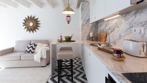 Una cocina moderna con encimera de mármol, horno empotrado y tostadora. Hay un taburete de bar y un sofá blanco con un cojín decorativo.