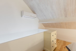 Ein Zimmer mit weißer Wand, einem weißen Schrank mit Schubladen und einer Decke mit Holzbalken.