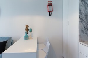 Een witte eettafel met twee stoelen, een blauwgroene vaas en een klein beeldje.
