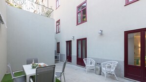 A courtyard with a table and chairs, a trash bin, and a small garden area.