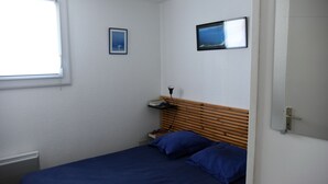 A small, neatly arranged bedroom with a single bed, a nightstand, a window, and two framed pictures on the wall. - 1 Bedroom Villa in SAINT CYPRIEN PLAGE (SAINT CYPRIEN PLAGE)