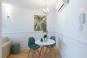 A modern dining area with a white table, teal chairs, a chandelier, and a tropical-themed painting on the wall. - Loureiro Villas - D (Oporto)