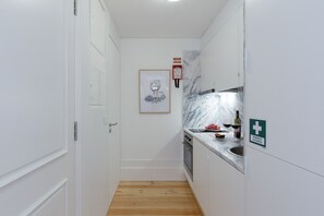 A narrow kitchen with white cabinetry, a marble backsplash, and a wooden floor. There is a framed artwork on the wall and a sign indicating the first floor.