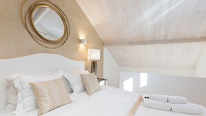 A bedroom with a bed, pillows, a round mirror, and a nightstand with a lamp.